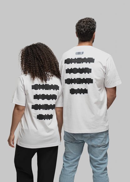 Das Bild zeigt zwei Personen von hinten, die nebeneinander stehen. Beide tragen weiße T-Shirts mit identischem Rückendruck: Vier gestapelte Textzeilen in schwarzer, verzerrter Blockschrift zeigen den Slogan „CHEAT YOUR CHEAT DAY“. Über dem Text befindet sich bei beiden ein minimalistischer Barcode mit kleiner Schrift. Die Person links hat mittellange, lockige Haare und trägt eine schwarze Hose, die rechte Person kurze dunkle Haare und eine helle Jeans. Hintergrund ist neutral hellgrau.