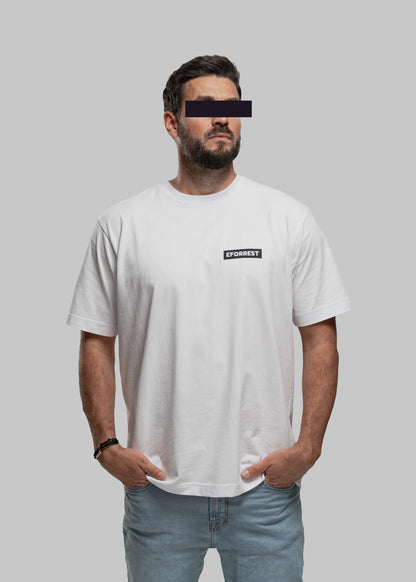 Auf dem Bild steht eine männlich gelesene Person vor neutralgrauem Hintergrund. Sie trägt ein locker geschnittenes weißes T-Shirt mit einem kleinen schwarzen EFORREST-Schriftzug in Großbuchstaben auf der linken Brust. Das Gesicht ist teilweise anonymisiert: Die Augenpartie ist mit einem schwarzen Balken zensiert. Die Person hat beide Hände in den Hosentaschen und trägt eine helle Jeans sowie ein Armband am linken Handgelenk. Der Stil ist modern, schlicht und streetwear-inspiriert.