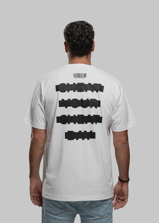 Die abgebildete Person steht mit dem Rücken zur Kamera und trägt ein weißes Oversized-T-Shirt. Der schwarze Aufdruck auf dem Rücken besteht aus vier versetzt gesetzten Textzeilen in grober Blockschrift: „CHEAT YOUR CHEAT DAY“. Über dem Text befindet sich ein minimalistischer Barcode mit kleiner Aufschrift. Die Person hat dunkelbraune, kurze Haare und trägt eine hellblaue Jeans. Der Hintergrund ist neutral hellgrau.