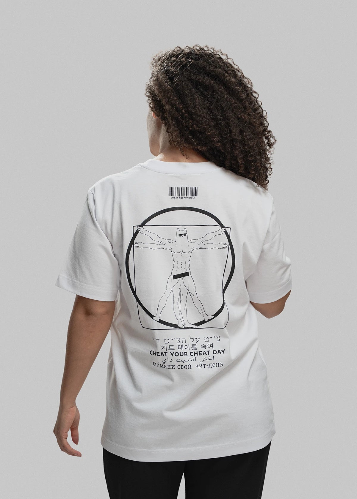 Eine Frau mit lockigem Haar trägt ein weißes T-Shirt. Auf der Rückseite ist ein großflächiger schwarzer Print zu sehen, der Leonardo da Vincis "Vitruvianischen Menschen" persifliert: Statt eines nackten Mannes mit offenen Armen ist eine muskulöse Comicfigur mit Maske (ähnlich einem Superhelden) in derselben Pose abgebildet. Über dem Motiv befindet sich ein Barcode mit der Aufschrift „CHEAT RESPONSIBLY“. Unter der Illustration steht in sieben verschiedenen Sprachen (u. a. Hebräisch, Koreanisch, Arabisch, Rus