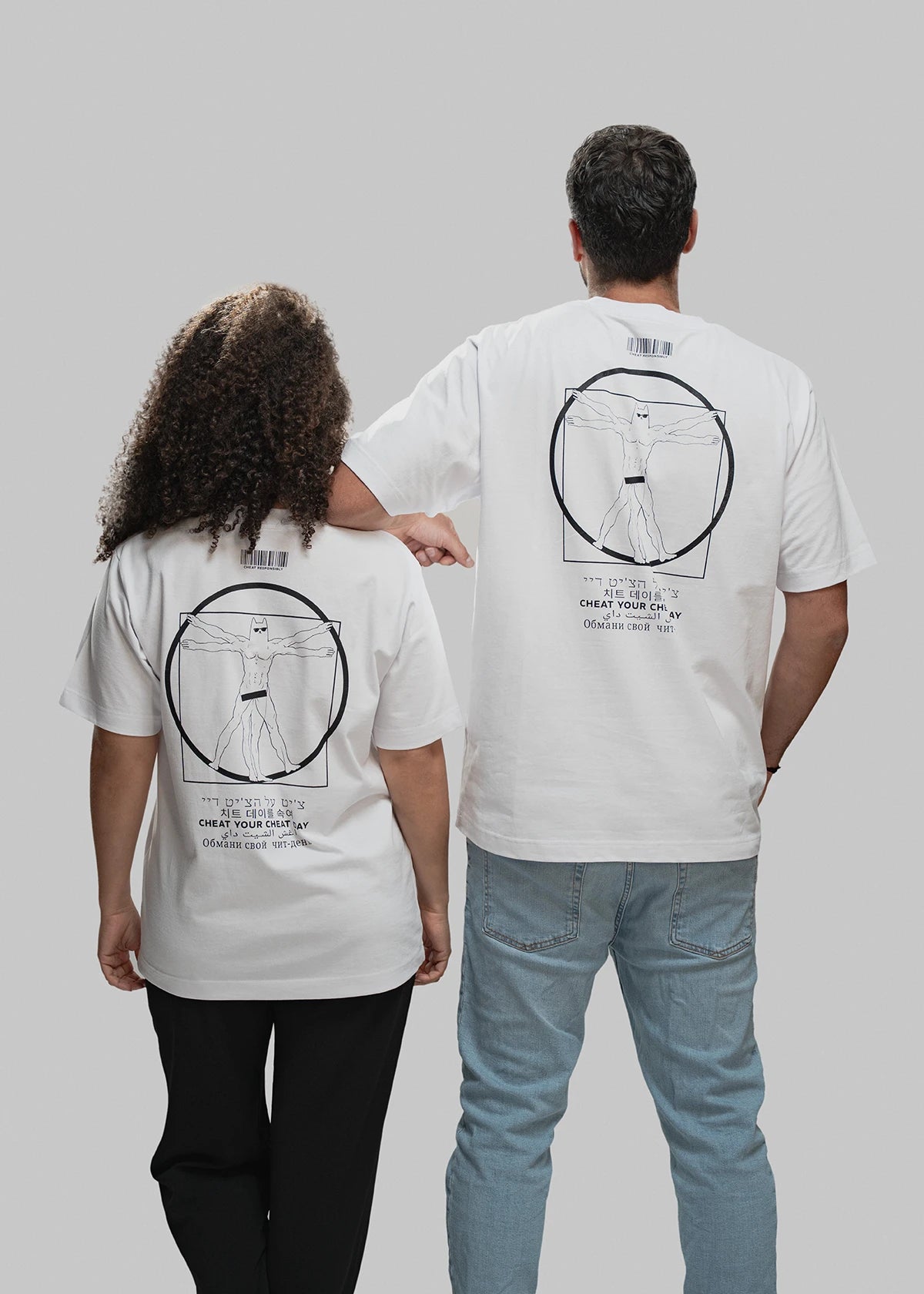 Das Bild zeigt zwei Personen von hinten vor grauem Hintergrund. Beide tragen weiße T-Shirts mit einem schwarzen, zentral platzierten Druck auf dem Rücken. Dieser zeigt eine an Leonardo da Vincis „Vitruvianischem Menschen“ angelehnte Figur mit Maske und Sixpack in einem Kreis und Quadrat. Unterhalb des Motivs steht der Claim „CHEAT YOUR CHEAT DAY“ in sechs verschiedenen Sprachen. Über dem Motiv befindet sich ein minimalistischer Barcode. Die linke Person trägt schwarze Hose und hat mittellanges, lockiges Haa